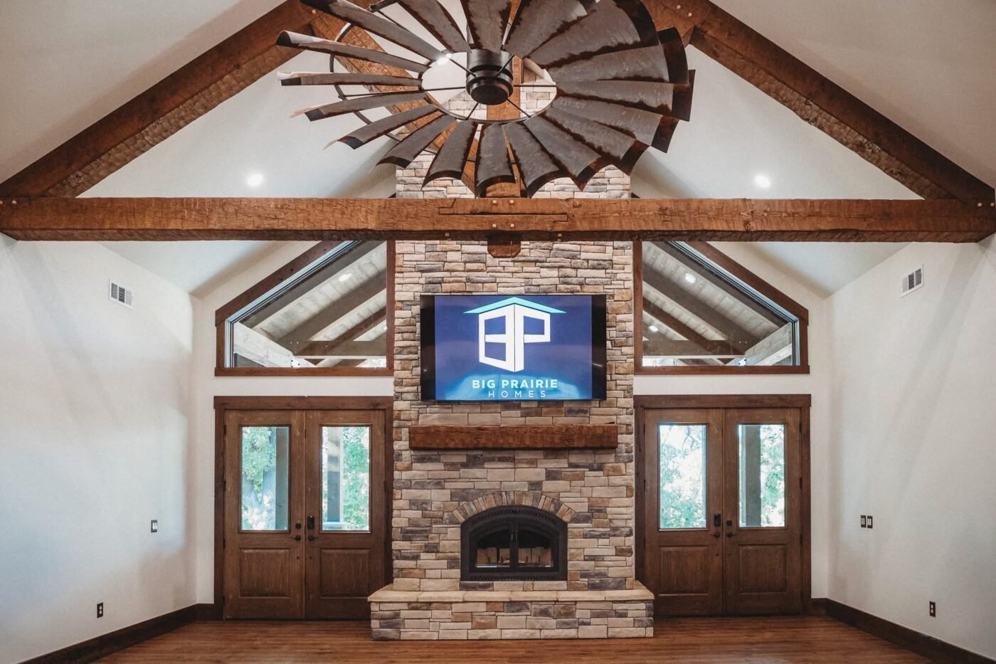 Interior of a newly finished home with a vaulted ceiling, exposed timber trusses, a windmill-style ceiling fan and a stone fireplace